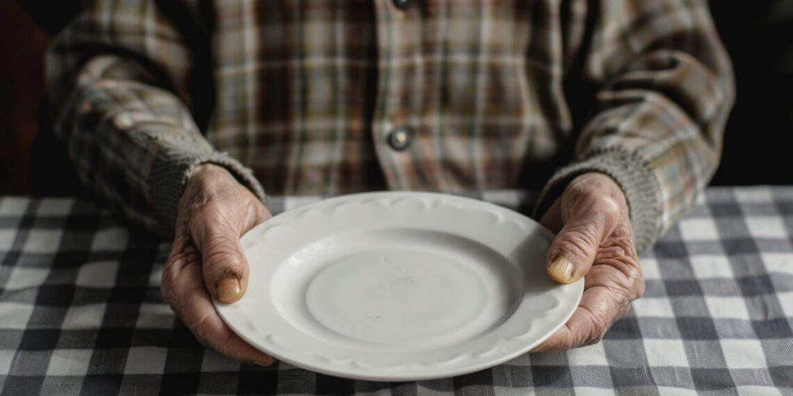 Old person in front of an empty plate , elders poverty and undernutrition concept image with a mature person with nutritional deficiencies