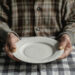 Old person in front of an empty plate , elders poverty and undernutrition concept image with a mature person with nutritional deficiencies